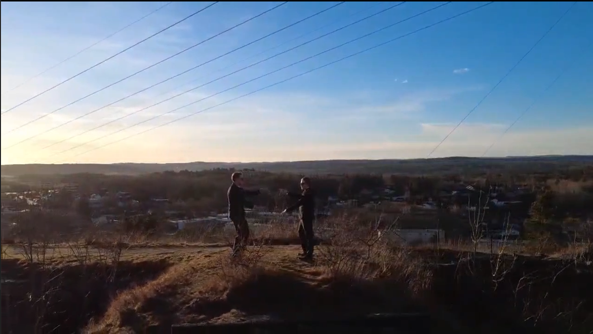 Bilde fra det ene droneklipped, to personer står foran solen og danser